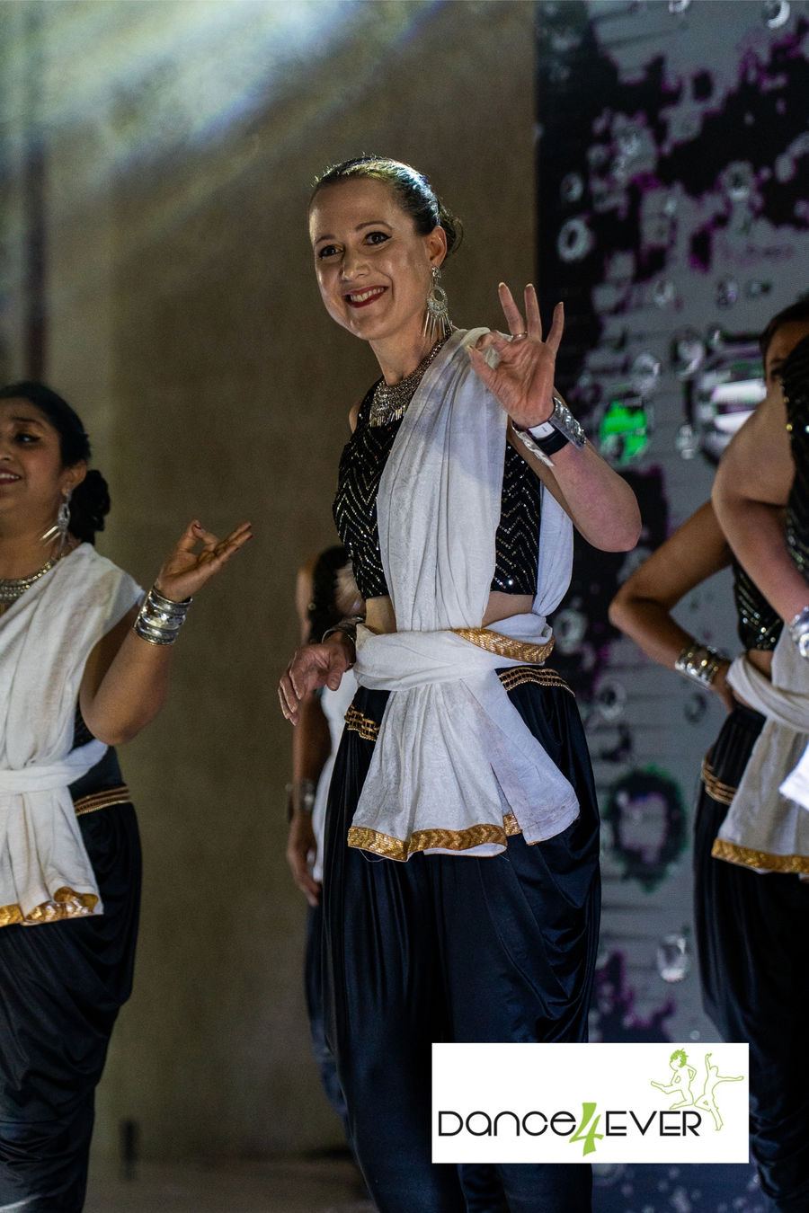 A smiling Dance4Ever student in white and navy classical costume mid performance